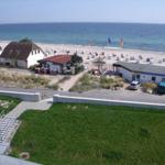 Strand mit Liegestühlen, Häuser und Grünflächen im Hintergrund.