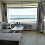 Wohnzimmer mit Sofa, Tisch und Meerblick über Balkon.