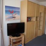 Ein Zimmer mit TV, Holzschrank und Wandbild eines Bootes am Strand.
