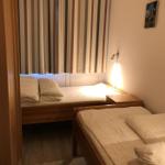 Zwei Einzelbetten mit Holzgestell und Bettwäsche. Streifenstore und Wandlampe.