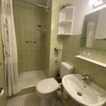 Badezimmer mit Dusche, Toilette und Waschbecken. Wandfliesen und Spiegel sichtbar.