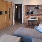 Wohnung mit Küche, Essplatz und Schlafbereich. Holzmöbel und helles Ambiente.