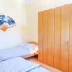 Zimmer mit zwei Betten, Holzschrank und Wandbild in Fächerform.