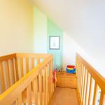 Kinderzimmer mit Holzgeländer, farbigen Wänden und Spielzeug auf einem Schrank.