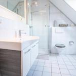 Badezimmer mit Dusche, Waschbecken und Toilette unter Dachschrägen.