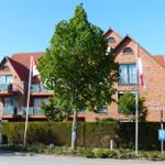 Villa Seewind mit rotem Dach und Balkonen. Vorderhof mit Bäumen und Hecke.