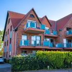 Rotes Backsteinhaus mit Balkonen und grünen Hecken im Vordergrund.