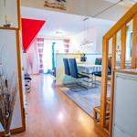 Haus mit Essbereich, Küchenzeile und Holzboden. Rote Wand und Fenster mit Vorhängen.