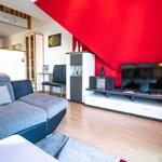 Wohnzimmer mit Sofa, Fernseher und roter Wand unter Dachschräge.