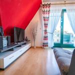 Wohnzimmer mit TV, Sofa und Balkon. Rote Wand und Holzboden.