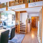 Küche mit Essbereich, Holztreppe und Obergeschoss mit Sitzgelegenheit.