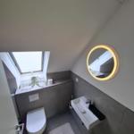 Badezimmer mit Dachfenster, runden Spiegel und Toilette.
