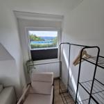 Raum mit Sessel, Kleiderständer und Fensterblick auf Gebäude und Bäume.