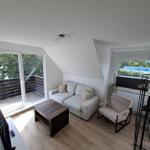 Wohnzimmer mit Sofa, Sessel und Tisch. Balkon und Fenster mit Blick.