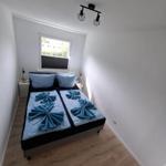 Schlafzimmer mit Doppelbett, Fenster und Holzboden. Blaue Bettwäsche und Nachttische.