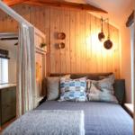 Bedroom with wooden wall, bed, and curtains. Two lamps hang on the wall.