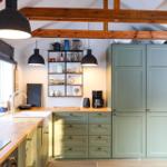 Kitchen with green cabinets, wooden countertop, and black pendant lights under wooden beams.