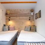 Two beds with pillows are against a wooden wall with shelf and lamps.