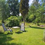 Garden with two recliners and table. Lawn area, trees, and shrubs surround the space.