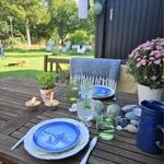 Garden table with table setting, flowers, and stones. Background with garden furniture and trees.