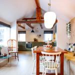 Dining area with wooden table, bench, and kitchen area in the background.
