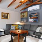 A living room with a gray sofa, two chairs, and a wooden table. Shelves on the wall hold books and games.