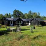 Black wooden cabin with garden and seating areas under blue sky.