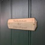 Holztafel mit Aufschrift: Velkommen Til Strandhuset an einer grünen Tür.