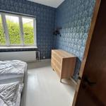Bedroom with blue patterned wallpaper, bed, dresser, and window overlooking greenery.