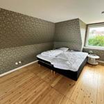 Bedroom with wooden floor, patterned wall covering, and window overlooking greenery.