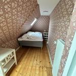Bedroom with wooden floor, patterned wallpaper, and sloped ceiling. Bed, nightstand, and radiator.