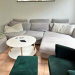 Living room with gray sofa, green armchair, round table. White brick wall and stained glass window.