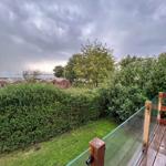 Deck with glass railing overlooking green areas and red houses.