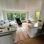 Living area with sofa, armchair, and large window overlooking green outdoor space.