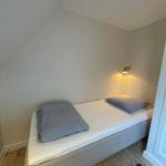 A bedroom with sloped ceiling, bed, wall lamp, and wooden floor.