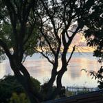 View through trees to a lake at sunset with gentle waves and a white fence.