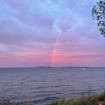 A rainbow in the sky over the sea, a small boat is visible in the background.