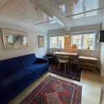 A room with blue sofa, table, chair and two rugs. Pictures hang on the wall.