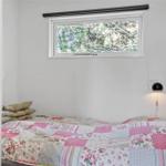 Schlafzimmer mit Bett, Fenster und Wandlampe. Decke mit Patchwork-Muster.