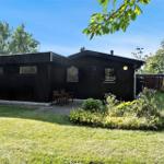 Schwarzes Holzhaus mit Garten, Sitzgelegenheit und Satellitenschüssel.