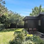 Ein dunkles Holzhaus mit Garten, zwei Stühlen und Bäumen im Hintergrund.