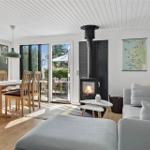 Wohn- und Essbereich mit Kamin, Sofa und Terrassentür. Holzboden und große Fenster.