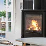 Ein Kaminofen mit brennendem Holz steht vor einer Glastür zum Garten.