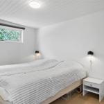 Schlafzimmer mit Bett, Nachttisch und Fenster. Wände und Decke sind weiß verkleidet.