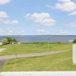 Weitläufiger Grünstreifen mit Blick auf das Meer und einige Häuser im Hintergrund.