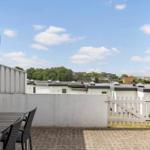 Terrasse mit Tisch und Stühlen, Blick auf Dächer und Bäume unter blauem Himmel.