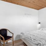 Schlafzimmer mit Bett, Stuhl und Fernseher an weißer Wand unter Holzdecke.