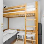 Zimmer mit Holz-Kojenbett, Stuhl und Kleiderhaken an der Wand.