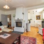 Wohnzimmer mit Kamin, rotem Sofa und Holzboden. Durchgänge zu weiteren Räumen.