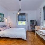 Schlafzimmer mit Bett, Sofa, TV und Holzboden. Fenster mit Jalousien und Wandbild.